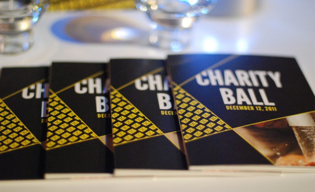 Black and gold Charity: ball program booklets on a table