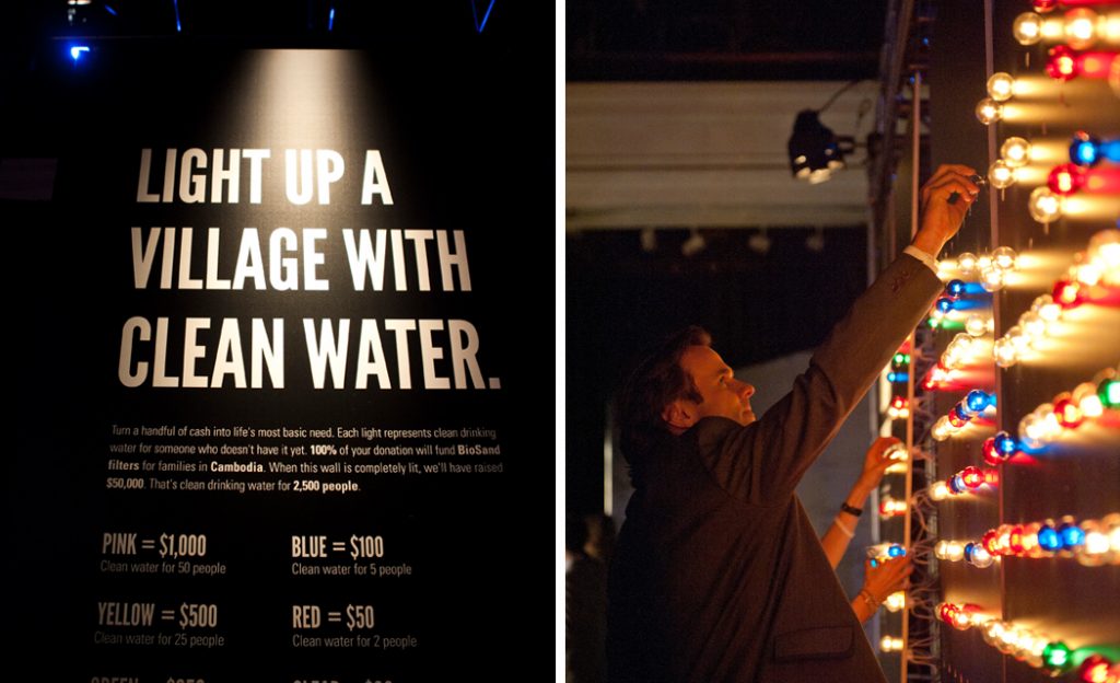 "Light up a village with clean water" sign and a guest adding lights to the bulb wall