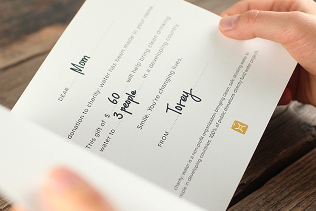 Hands holding a gift card letter reading "This gift of $60 will help bring clean drinking water to 3 people"