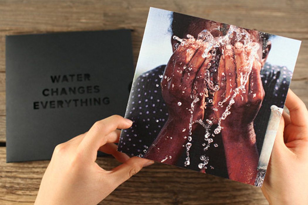 Hands holding a photograph of splashing water in front of the black "Water changes everything" folder