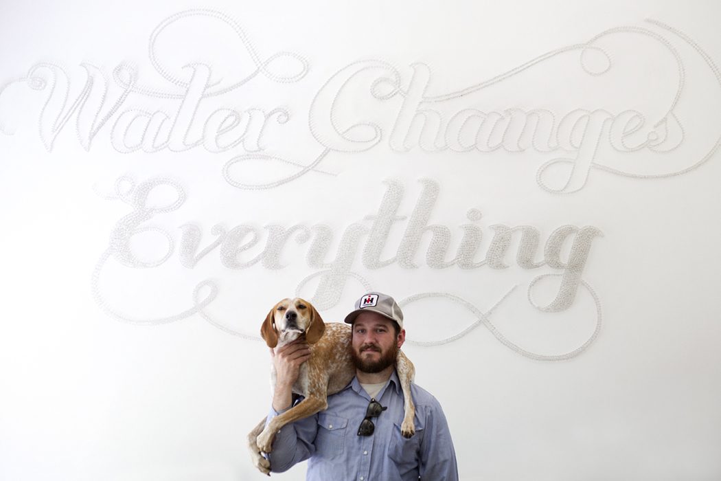 Embossed "Water changes everything" script on a white wall with a man holding a dog on his shoulders