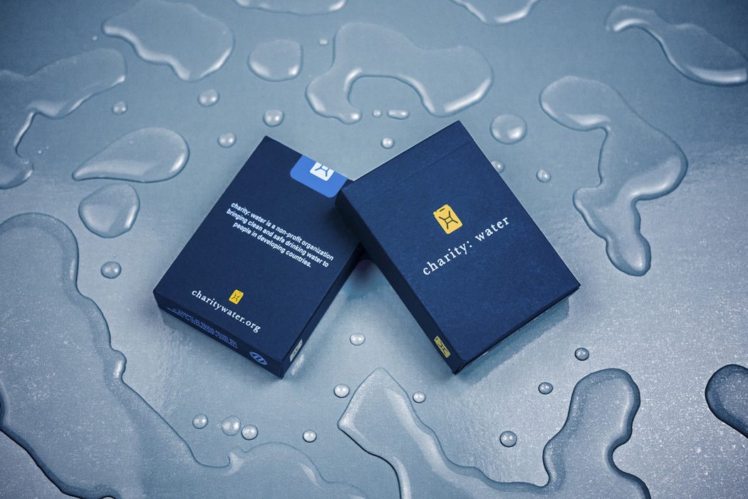Two navy charity: water playing card boxes on a wet blue surface