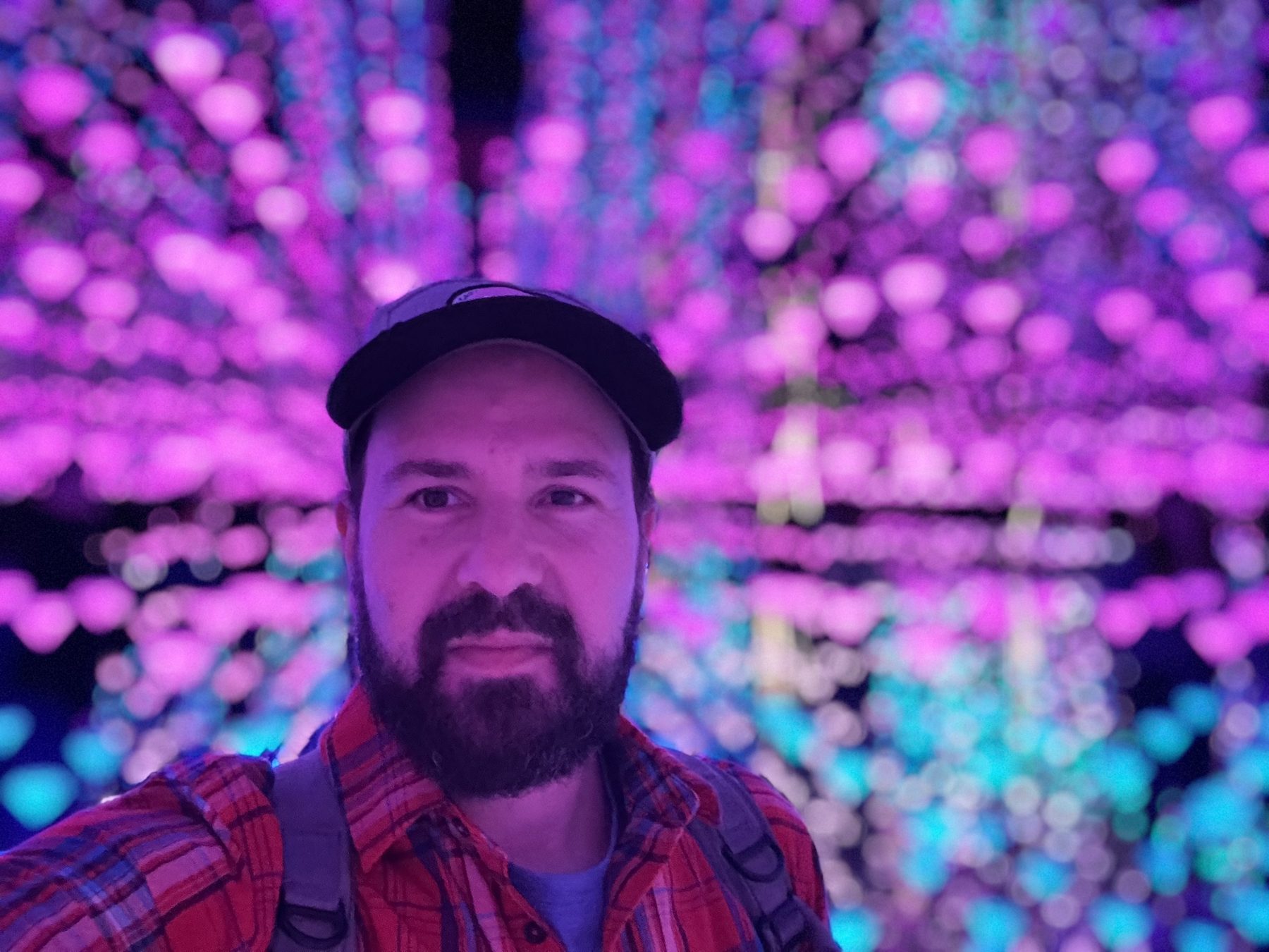 Greg in a cap and plaid shirt surrounded by glowing pink lights