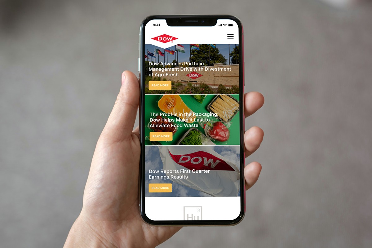 Hand holding a phone that shows the redesigned Dow.com home page with three news tiles and a search bar